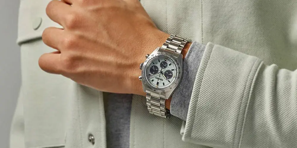 Muñeca de hombre con un cronógrafo SEIKO Prospex Speedtimer de esfera clara y malla de acero, sobre una camisa verde agua